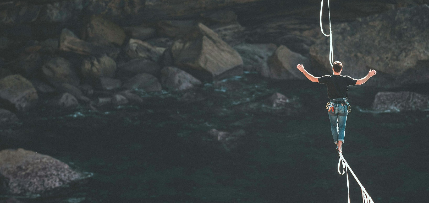 A person walks on a tightrope suspended over a river.